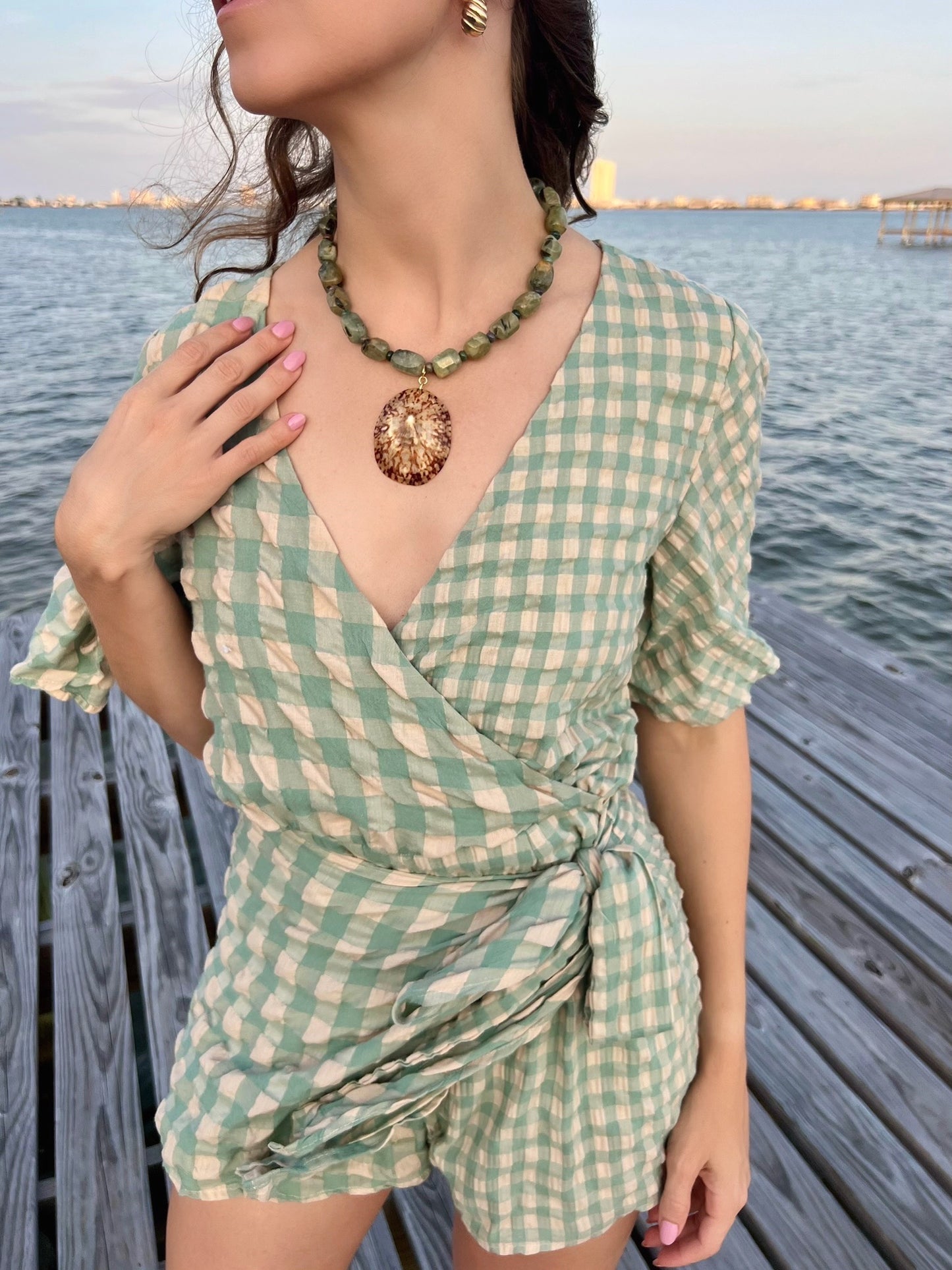 A lady wearing a green outfit with a necklace with green beads and a large brown pendant on a white background