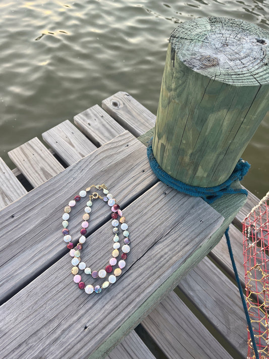 Multicolored coin freshwater pearl necklace laying on a dock surrounded by a lake