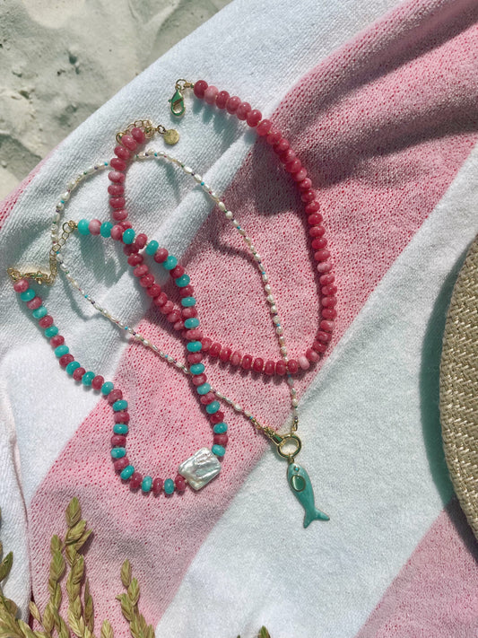 Three beaded necklaces laying on a pink and white striped beach towel.