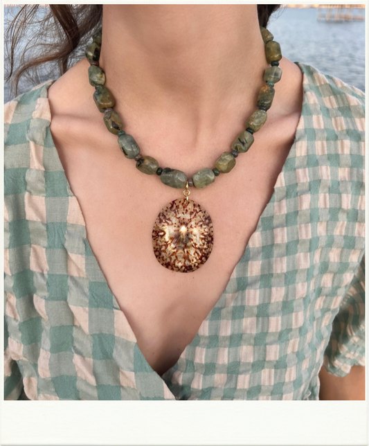 Close up of a lady wearing a necklace with green beads and a large brown shell pendant