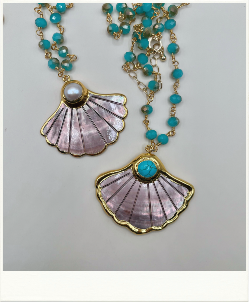 A gold-tone shell pendant necklace with turquoise beads, featuring two scalloped shell pendants with iridescent lavender-pink inlay and turquoise accents.
