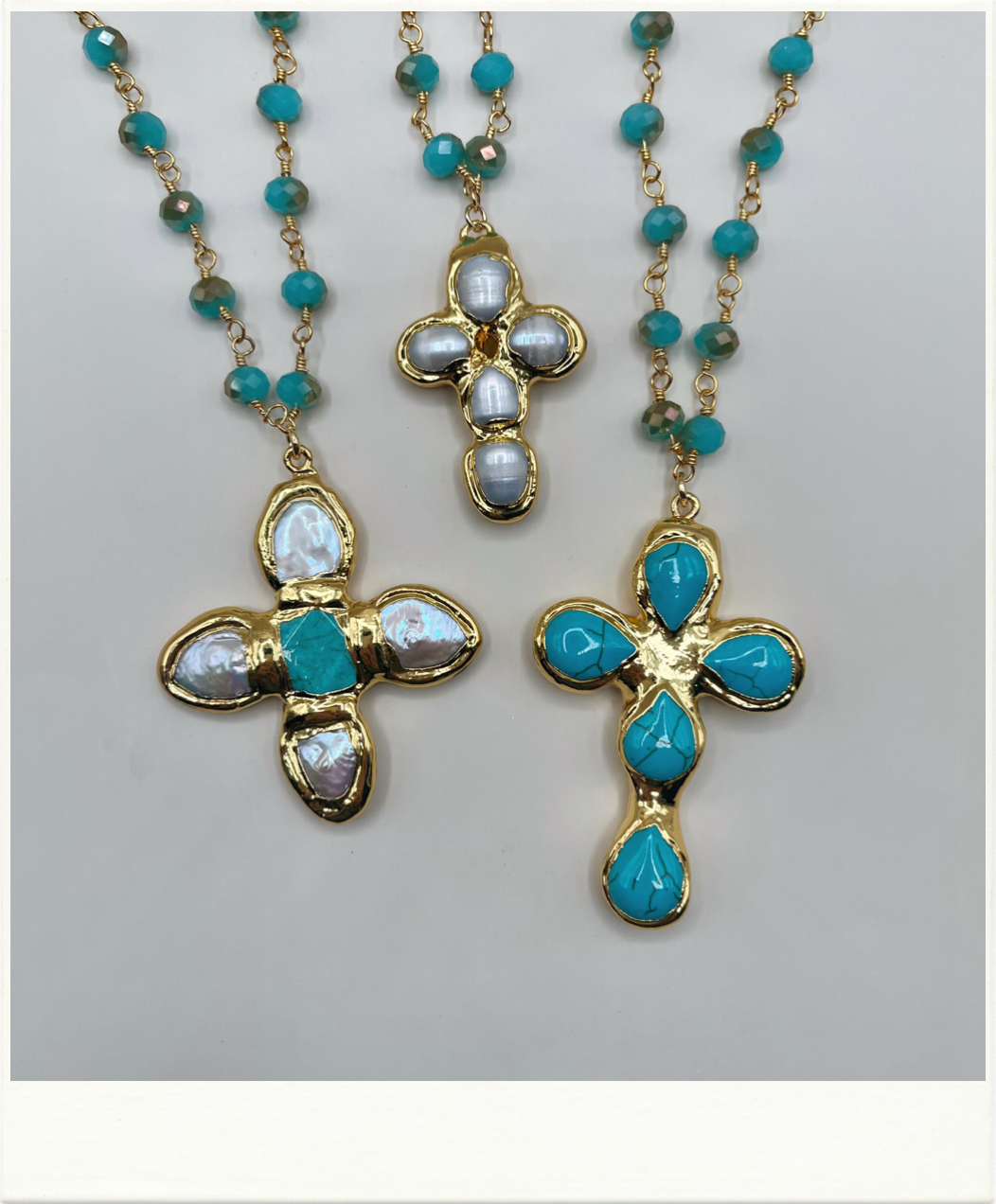 Three gold cross necklaces with turquoise and white opal-like stones, displayed on a light gray background.
