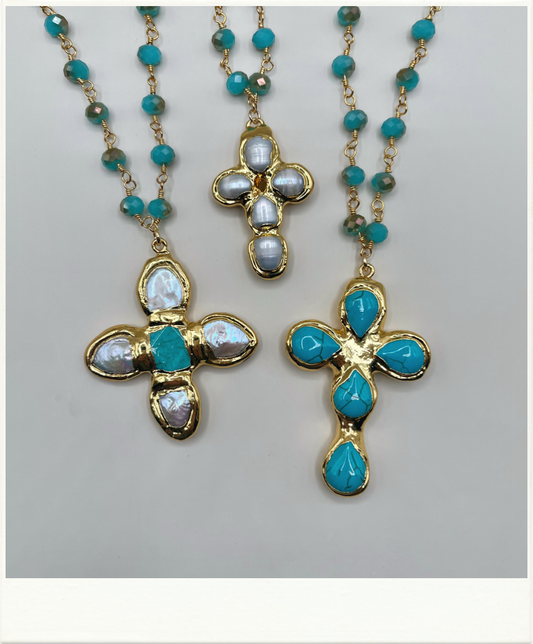 Three gold cross necklaces with turquoise and white opal-like stones, displayed on a light gray background.