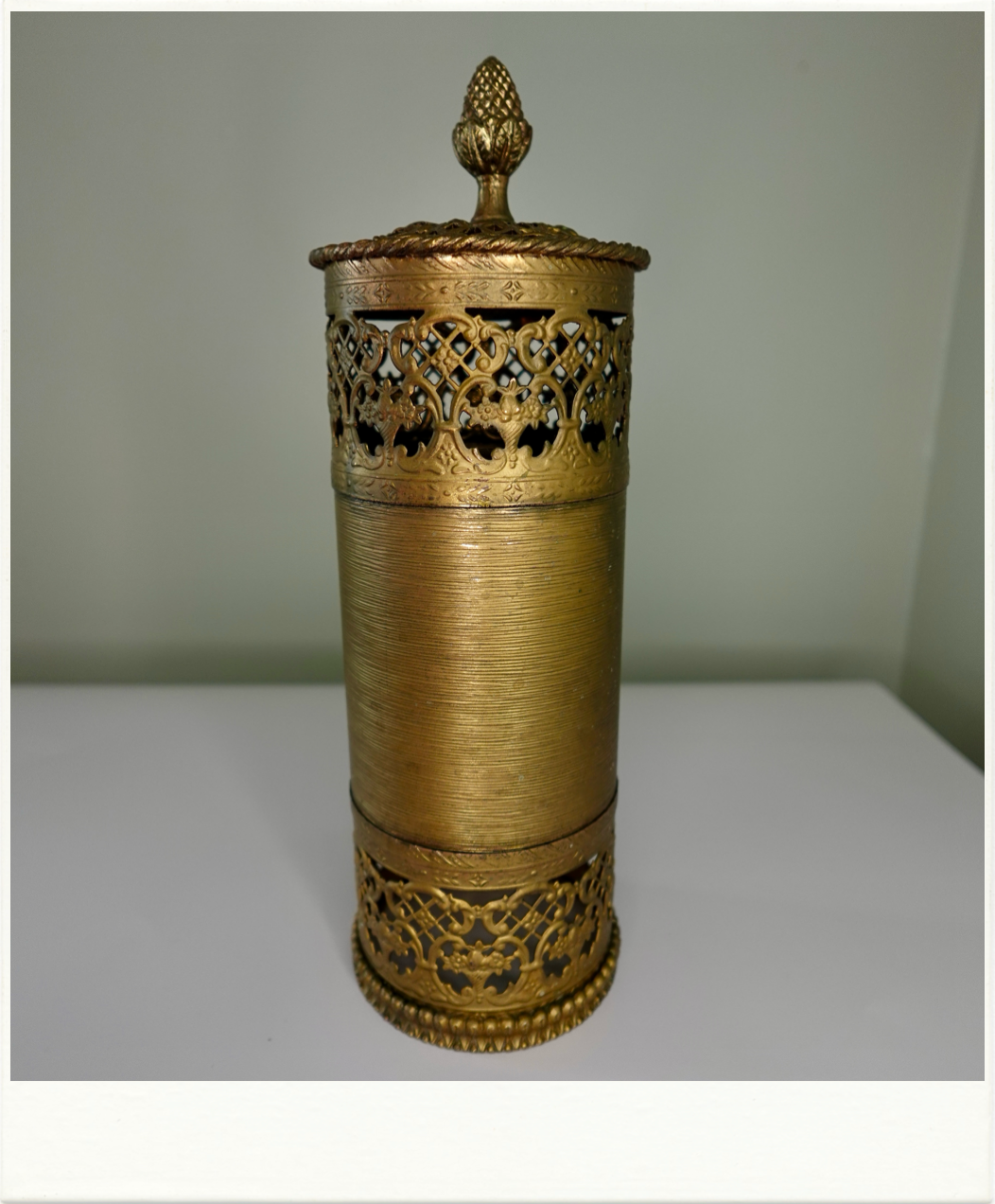 Tall vintage brass vanity container with ornate filigree trim and pineapple finial lid. Mid-century decorative accent or bathroom accessory from Birdie Street.