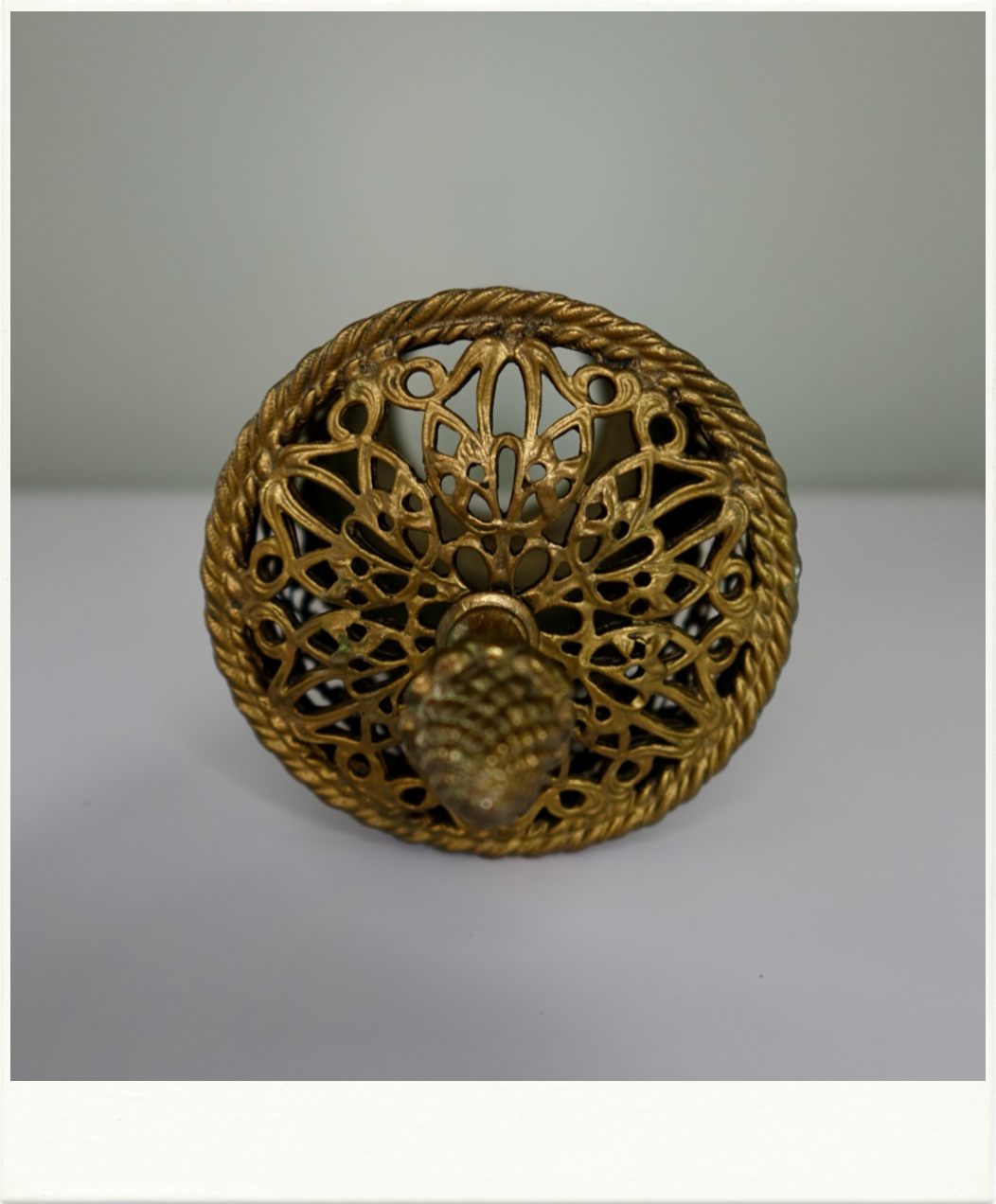 Top view of vintage brass vanity container lid with intricate filigree design and pineapple finial. Decorative mid-century metalwork from Birdie Street.