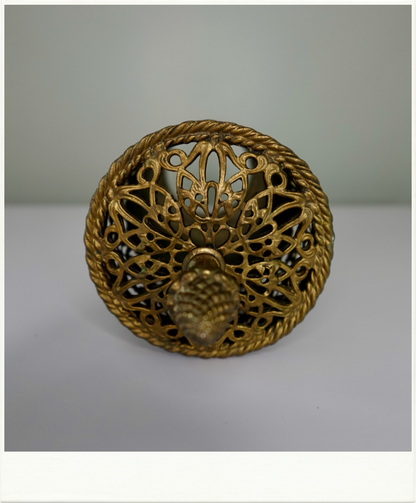 Top view of vintage brass vanity container lid with intricate filigree design and pineapple finial. Decorative mid-century metalwork from Birdie Street.