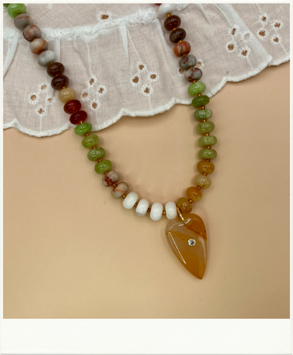 Necklace with multicolored beads and a large heart shaped orange stone pendant on a beige background.